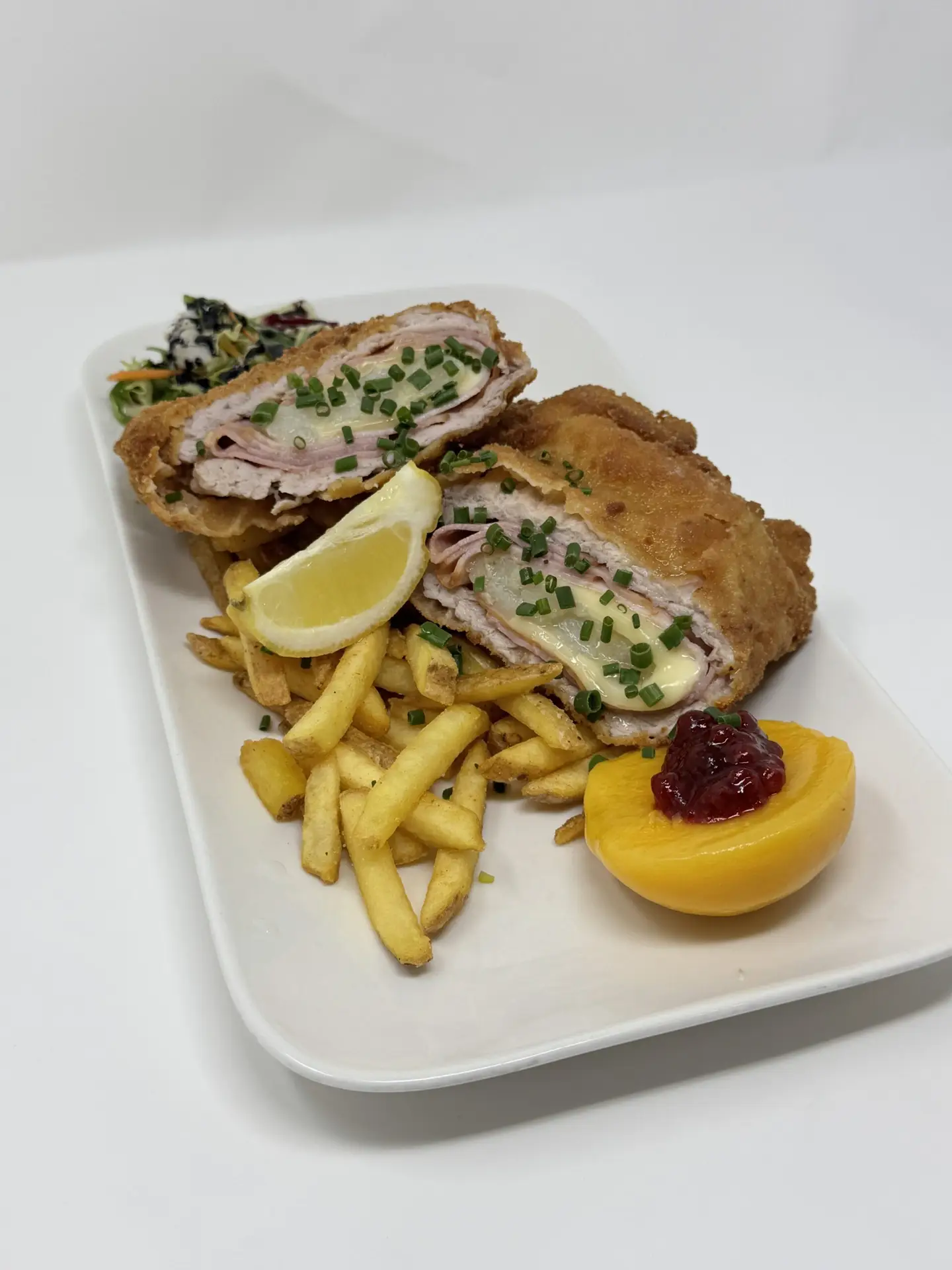 Cordon-Bleu, Schwein oder Huhn, mit Pommes, Zitronenspalte und Preiselbeer-Pfirsich